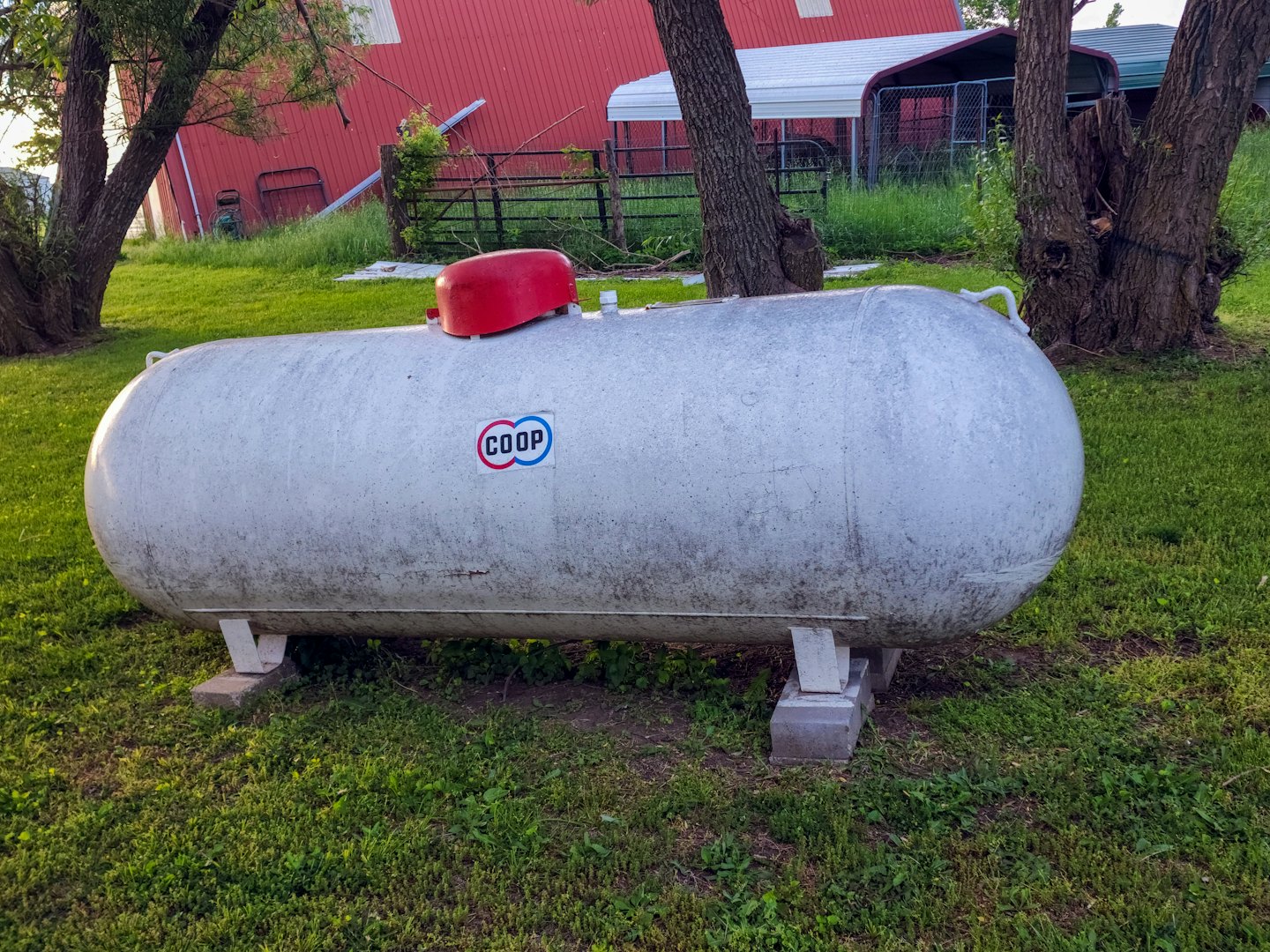 Propane tank on blocks in a green field with a barn.