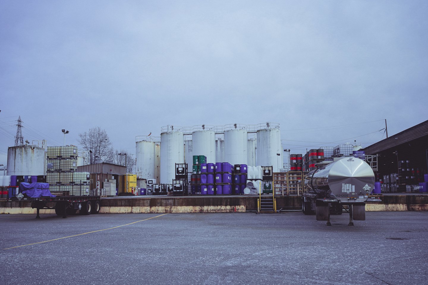 Industrial storage yard with tanks, barrels, and shipping trailers.