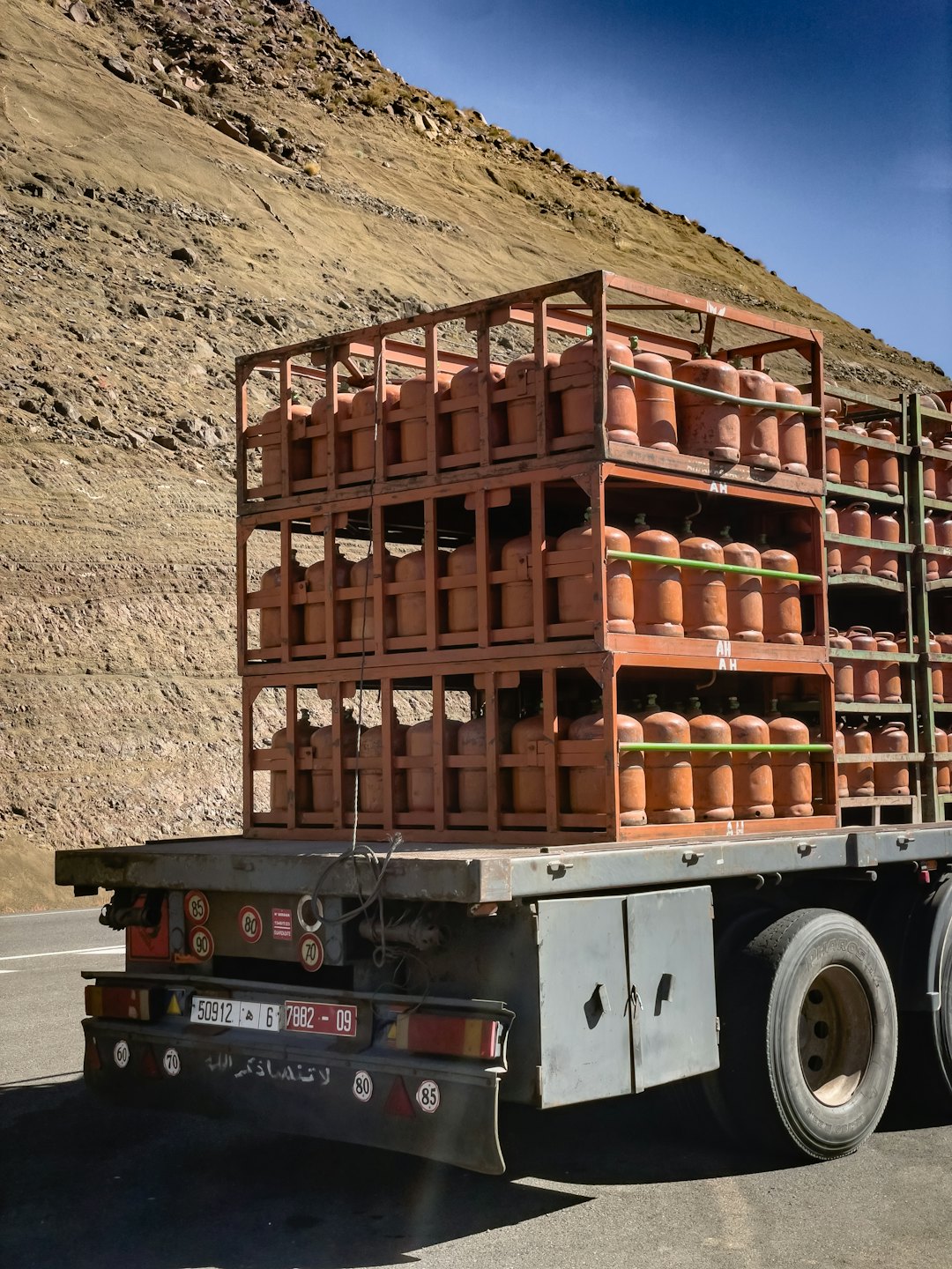 A flatbed truck transports gas cylinders past a rocky mountain.