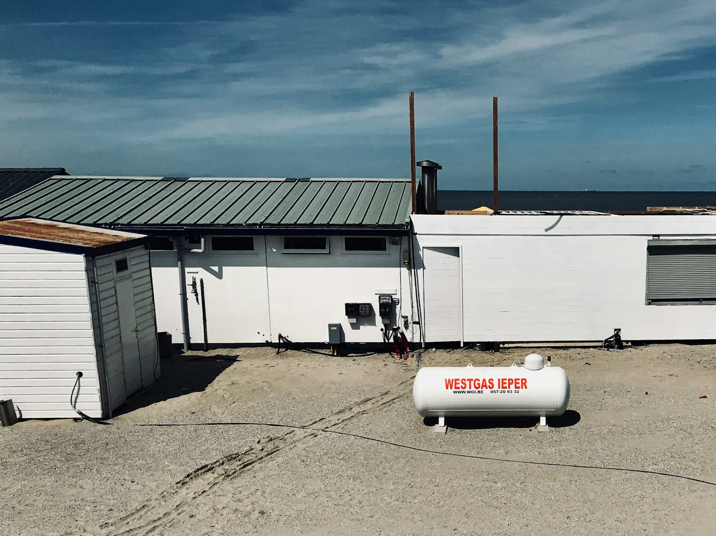 Propane tank sits on gravel before coastal industrial buildings.