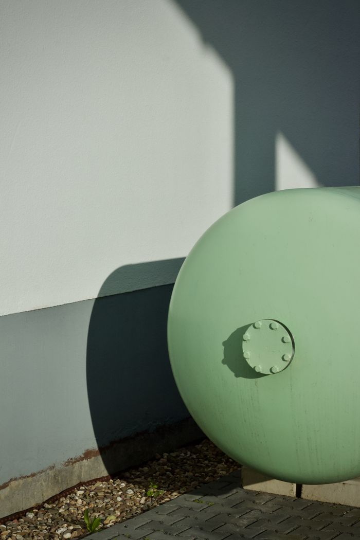 Abstract view of a green industrial tank against a white wall, casting shadows.