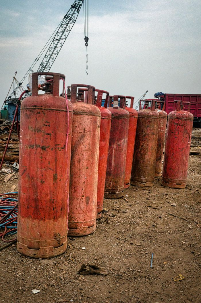 Lange aged red gas tanks placed on dry ground in industrial area in daytime